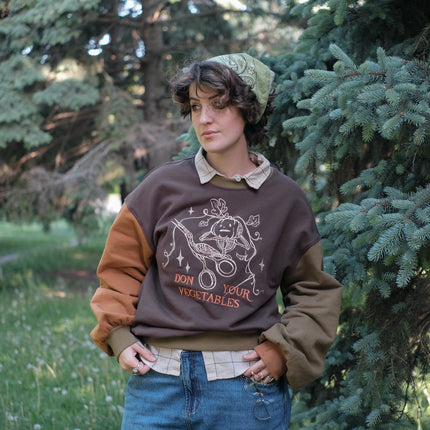 Cozy, oversized, puff-sleeved, cotton crewneck sweater in pumpkin-orange and shades of brown. The sweater features an intricately embroidered design in white and orange, of a pumpkin skeleton, vines, stork scissors, and reads “Don Your Vegetables”.