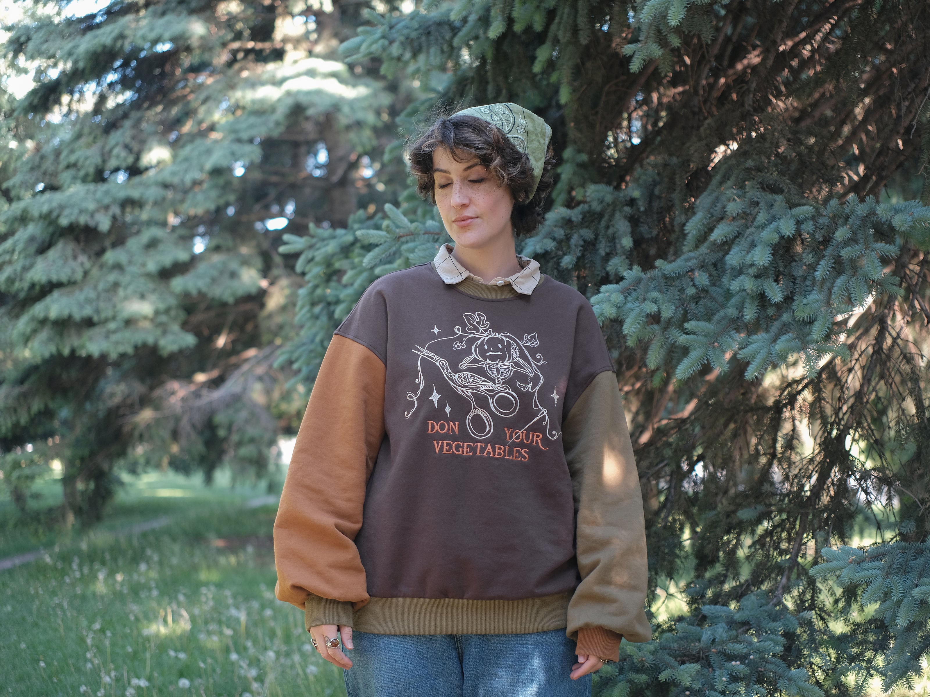 Cozy, oversized, puff-sleeved, cotton crewneck sweater in pumpkin-orange and shades of brown. The sweater features an intricately embroidered design in white and orange, of a pumpkin skeleton, vines, stork scissors, and reads â€œDon Your Vegetablesâ€.