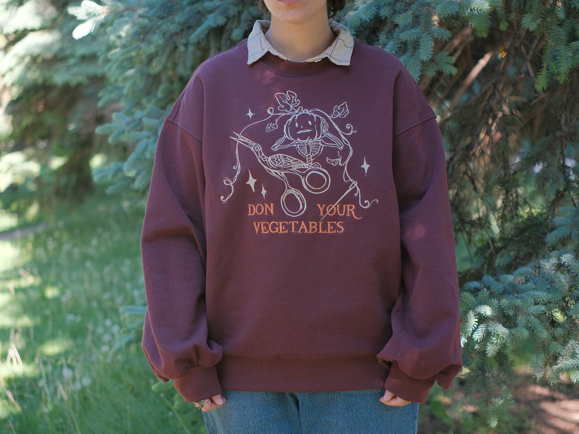 Cozy, oversized, puff-sleeved, cotton with fleece-lining, crewneck sweater in burgundy. The sweater features an intricately embroidered design in white and orange, of a pumpkin skeleton, vines, stork scissors, and reads â€œDon Your Vegetablesâ€.