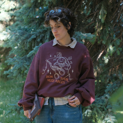 Cozy, oversized, puff-sleeved, cotton with fleece-lining, crewneck sweater in burgundy. The sweater features an intricately embroidered design in white and orange, of a pumpkin skeleton, vines, stork scissors, and reads â€œDon Your Vegetablesâ€.