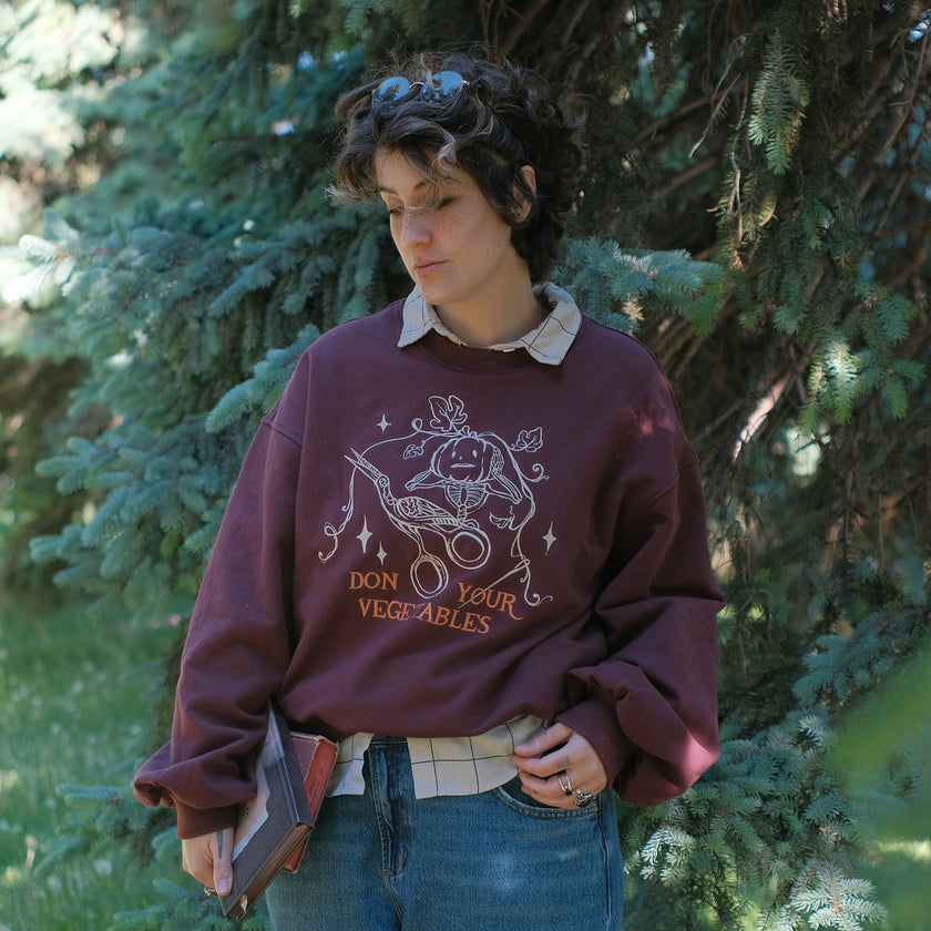 Cozy, oversized, puff-sleeved, cotton with fleece-lining, crewneck sweater in burgundy. The sweater features an intricately embroidered design in white and orange, of a pumpkin skeleton, vines, stork scissors, and reads â€œDon Your Vegetablesâ€.