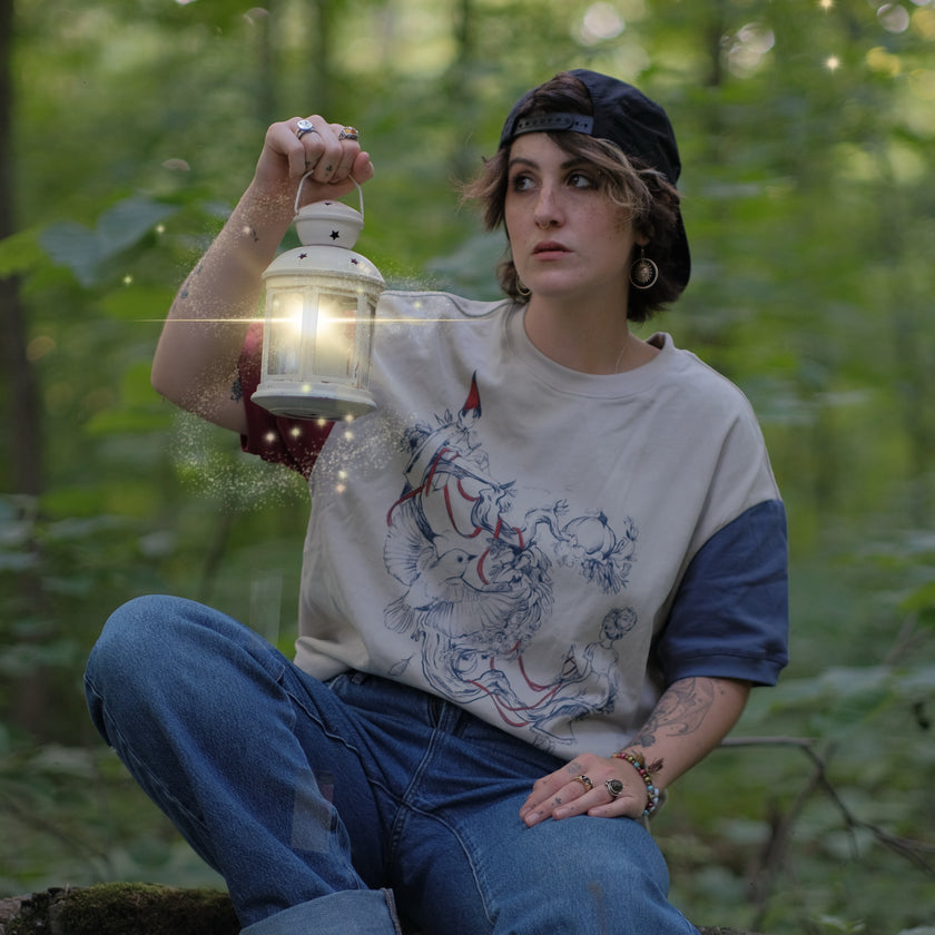 A cotton, vintage-style ringer t-shirt, in soft cream, and mismatched sleeves in red and navy. The shirt is printed with a tapestry inspired illustration including details of some young-lovers, a ripe pumpkin, sturdy tree branches, and a red ribbon.