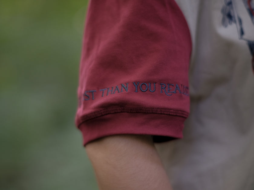 A cotton, vintage-style ringer t-shirt, in soft cream, and mismatched sleeves in red and navy. The shirt is printed with a tapestry inspired illustration including details of some young-lovers, a ripe pumpkin, sturdy tree branches, and a red ribbon.