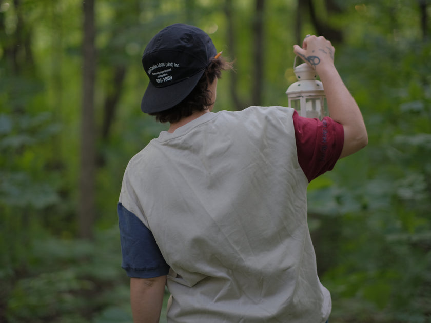 A cotton, vintage-style ringer t-shirt, in soft cream, and mismatched sleeves in red and navy. The shirt is printed with a tapestry inspired illustration including details of some young-lovers, a ripe pumpkin, sturdy tree branches, and a red ribbon.