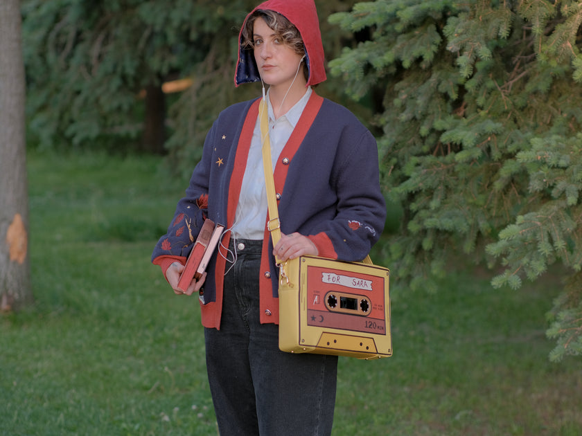 Orange and yellow backpack/satchel, designed to resemble a mix-tape, featuring the classic tape shape, and reads “For Sarah”. The bag includes 2 adjustable backpack straps and 1 adjustable cross-body strap, and features two inner pockets, a padded section, and pen straps. Inner fabric is custom-printed with a stain-resistant fabric.