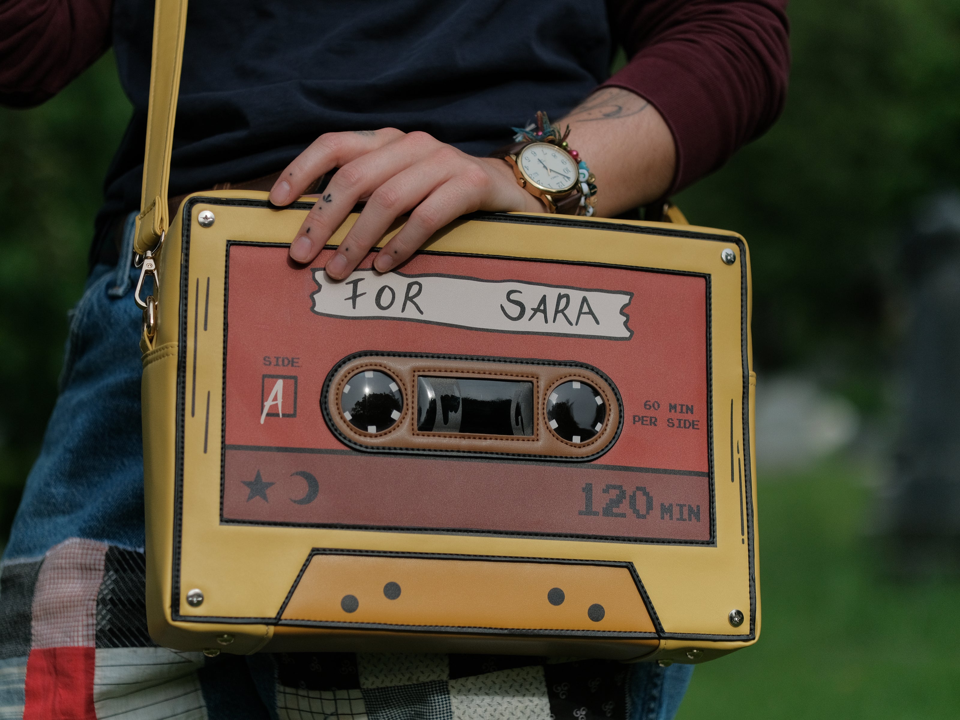 Orange and yellow backpack/satchel, designed to resemble a mix-tape, featuring the classic tape shape, and reads “For Sarah”. The bag includes 2 adjustable backpack straps and 1 adjustable cross-body strap, and features two inner pockets, a padded section, and pen straps. Inner fabric is custom-printed with a stain-resistant fabric.