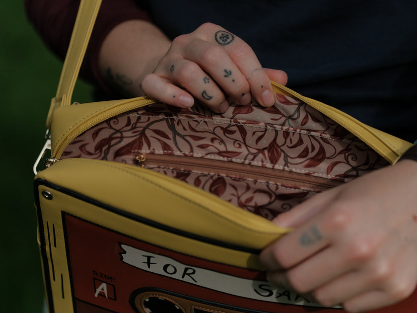 Orange and yellow backpack/satchel, designed to resemble a mix-tape, featuring the classic tape shape, and reads “For Sarah”. The bag includes 2 adjustable backpack straps and 1 adjustable cross-body strap, and features two inner pockets, a padded section, and pen straps. Inner fabric is custom-printed with a stain-resistant fabric.