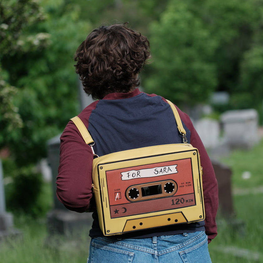 Orange and yellow backpack/satchel, designed to resemble a mix-tape, featuring the classic tape shape, and reads “For Sarah”. The bag includes 2 adjustable backpack straps and 1 adjustable cross-body strap, and features two inner pockets, a padded section, and pen straps. Inner fabric is custom-printed with a stain-resistant fabric.