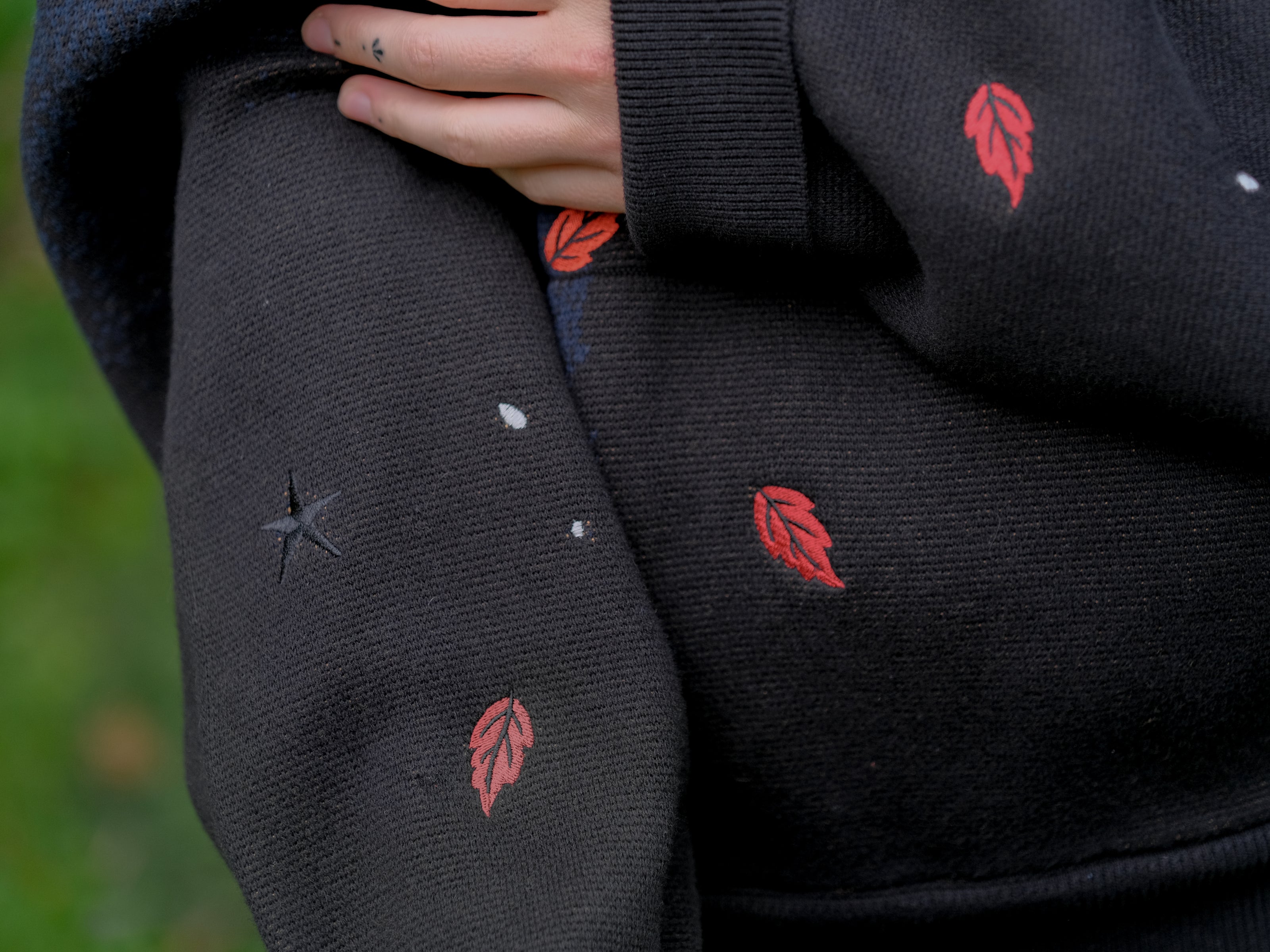 Cozy, cotton, knit hoodie in black and navy with red lining. The sweater features an intricately printed design of a beastly woodland creature, and is detailed with embroidered leaves, glowing eyes, melting snow, and lantern.