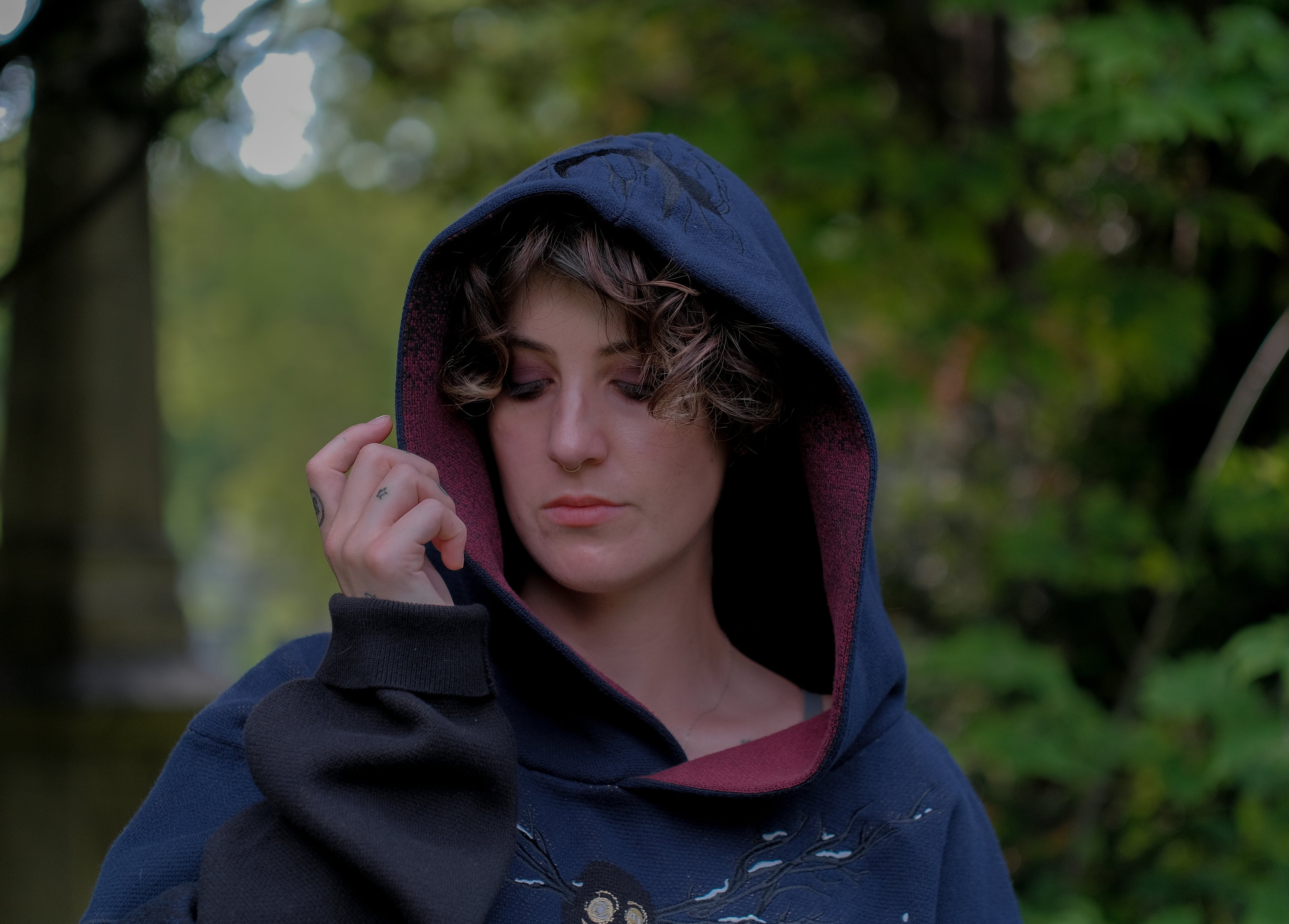 Cozy, cotton, knit hoodie in black and navy with red lining. The sweater features an intricately printed design of a beastly woodland creature, and is detailed with embroidered leaves, glowing eyes, melting snow, and lantern.