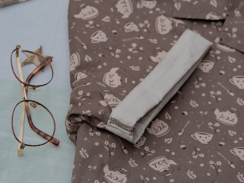 Warm, boba brown shade short-sleeve button up t-shirt printed with a whimsical pattern of the classic chubby teapot and matching cup, autumnal oak leaves, tea bag, spoon and sugar cubes. The shirt has a pyramid tea bag pocket, as well as a relaxed fit and rolled cuffs.