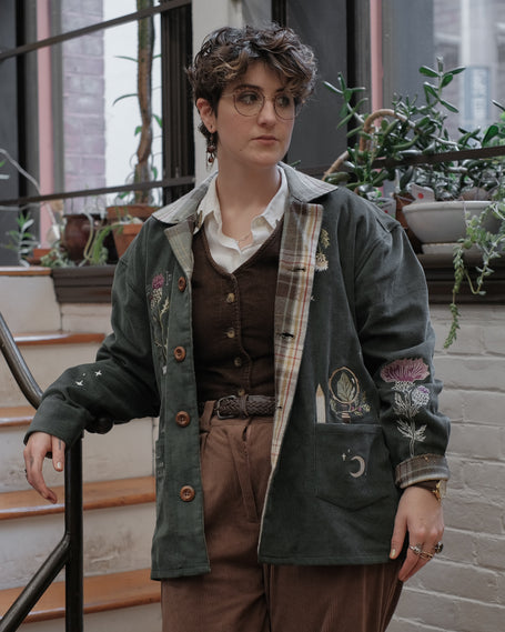 Dark green fall/spring button up corduroy jacket with soft brown plaid lining, featuring embroidered thistles, pollinators, and their Latin names.