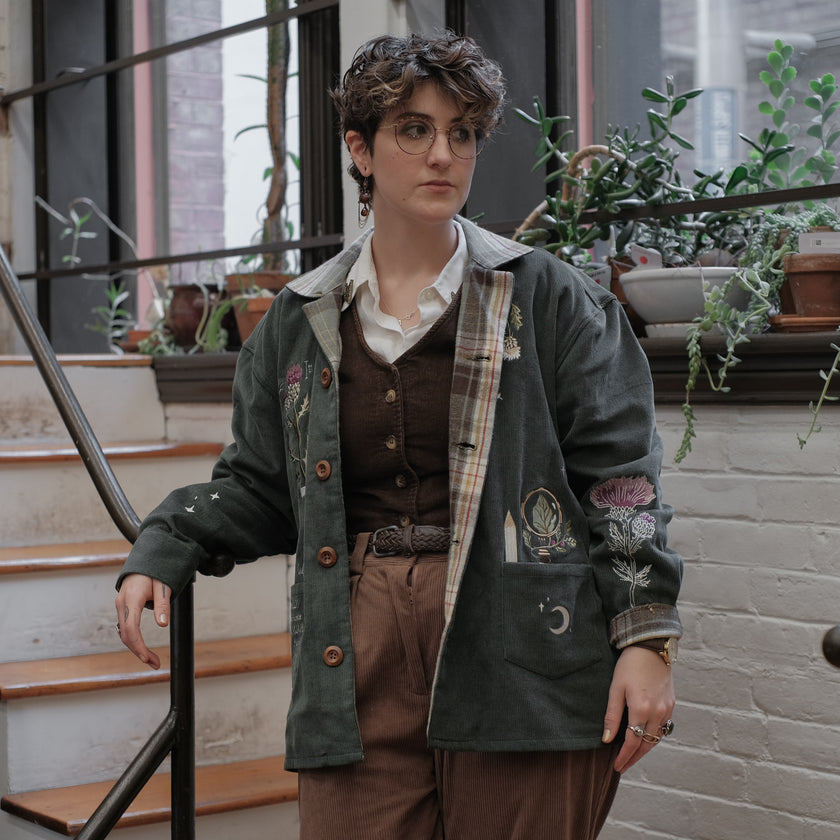 Dark green fall/spring button up corduroy jacket with soft brown plaid lining, featuring embroidered thistles, pollinators, and their Latin names.