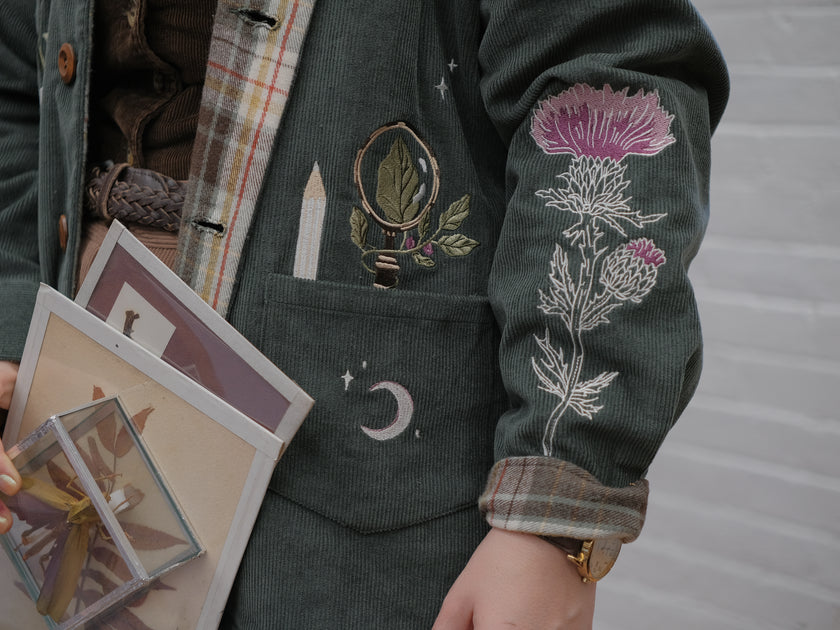 Dark green fall/spring button up corduroy jacket with soft brown plaid lining, featuring embroidered thistles, pollinators, and their Latin names.