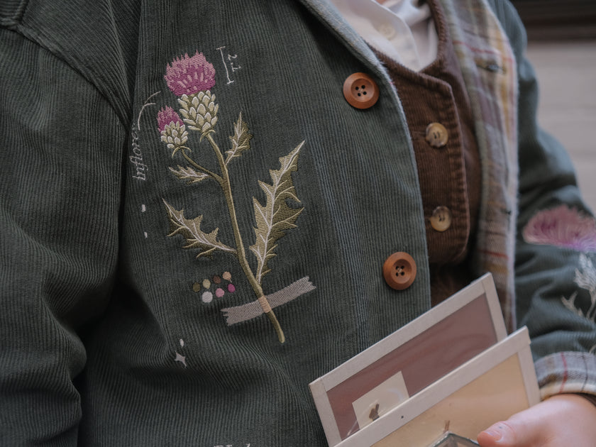 Dark green fall/spring button up corduroy jacket with soft brown plaid lining, featuring embroidered thistles, pollinators, and their Latin names.