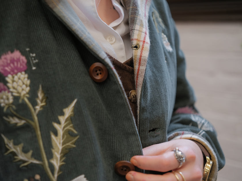 Dark green fall/spring button up corduroy jacket with soft brown plaid lining, featuring embroidered thistles, pollinators, and their Latin names.