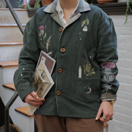 Dark green fall/spring button up corduroy jacket with soft brown plaid lining, featuring embroidered thistles, pollinators, and their Latin names.