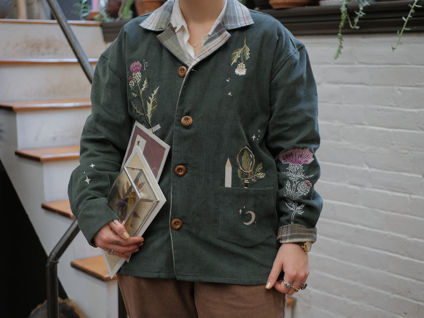 Dark green fall/spring button up corduroy jacket with soft brown plaid lining, featuring embroidered thistles, pollinators, and their Latin names.