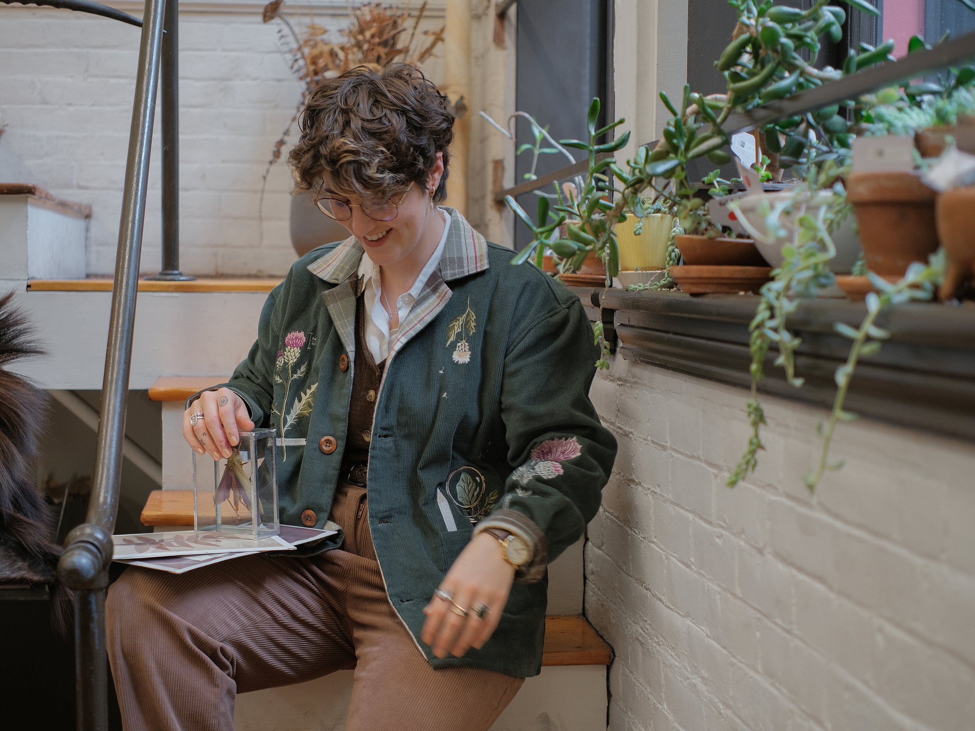 Dark green fall/spring button up corduroy jacket with soft brown plaid lining, featuring embroidered thistles, pollinators, and their Latin names.