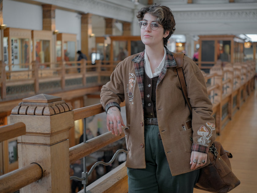Light brown corduroy  button up, Fall/spring jacket adorned with botanical and mycological illustrations, including mushrooms in a jar, latin nomenclature, and hand-drawn motifs. The jacket features green and red plaid accents on the collar and cuffs, along with functional pockets embroidered with nature-inspired designs.