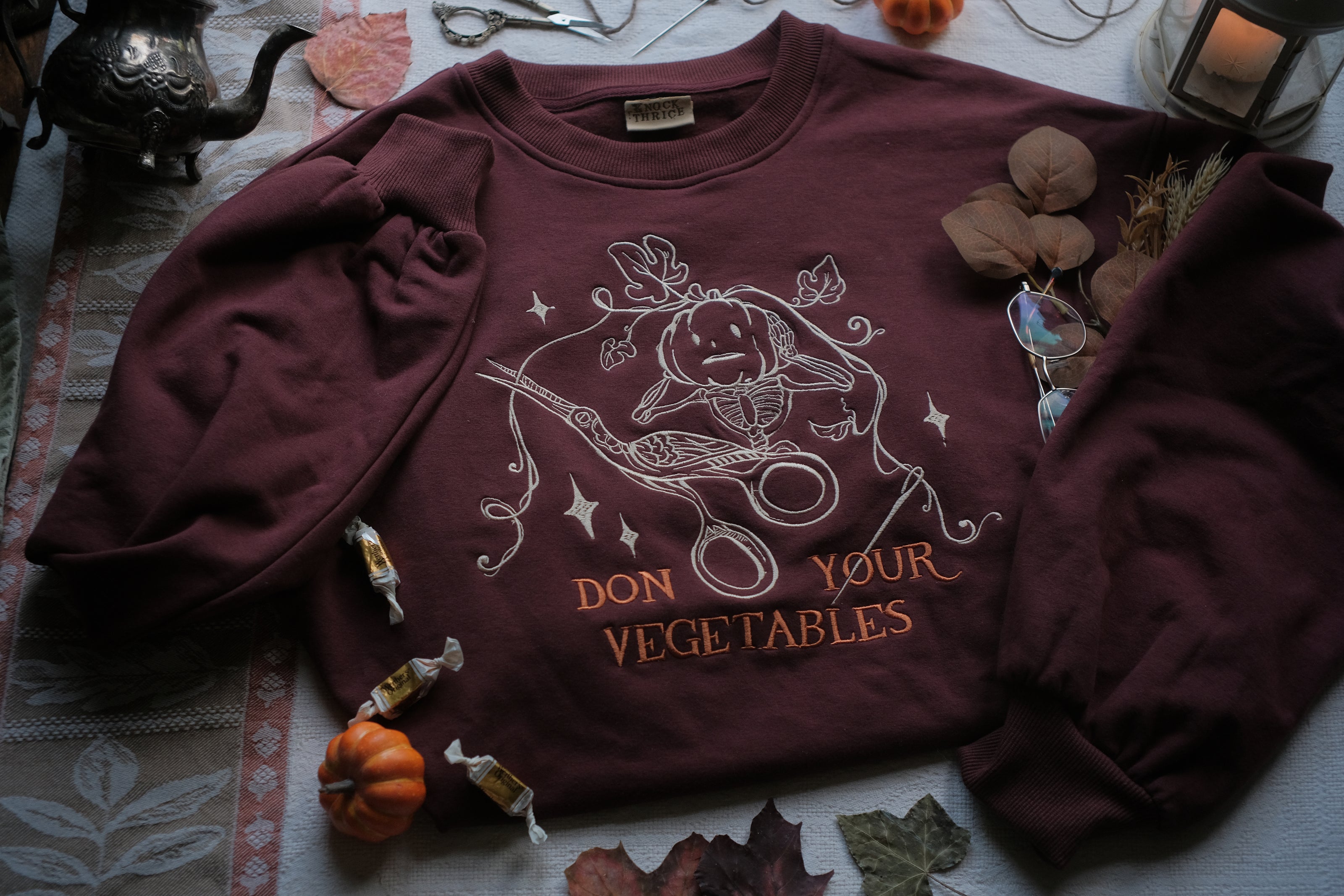 Cozy, oversized, puff-sleeved, cotton with fleece-lining, crewneck sweater in burgundy. The sweater features an intricately embroidered design in white and orange, of a pumpkin skeleton, vines, stork scissors, and reads â€œDon Your Vegetablesâ€.
