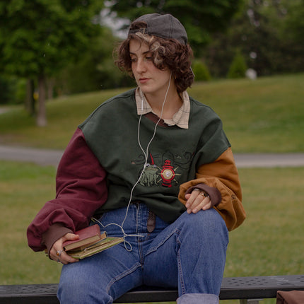 Cozy, oversized, puff-sleeved, color-blocked, cotton crewneck sweater in forest green, with burgundy, and mustard coloured sleeves. The sweater features an intricately embroidered design of a green frog with a red wizard hat and a red lantern on the chest.