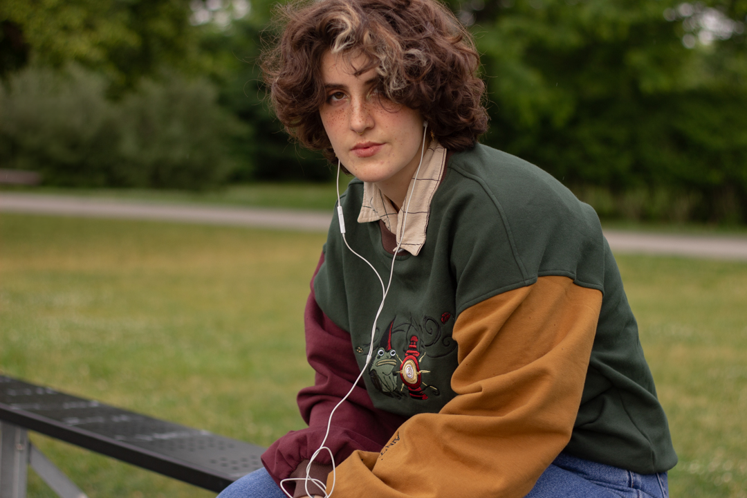 Cozy, oversized, puff-sleeved, color-blocked, cotton crewneck sweater in forest green, with burgundy, and mustard coloured sleeves. The sweater features an intricately embroidered design of a green frog with a red wizard hat and a red lantern on the chest.
