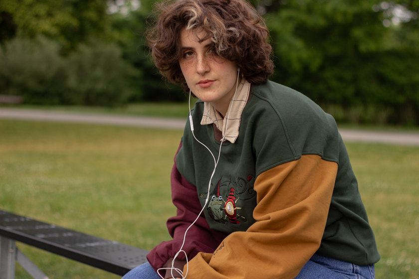 Cozy, oversized, puff-sleeved, color-blocked, cotton crewneck sweater in forest green, with burgundy, and mustard coloured sleeves. The sweater features an intricately embroidered design of a green frog with a red wizard hat and a red lantern on the chest.