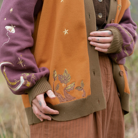 A 100% cotton, button-up, mulberry, chestnut-brown, and forest-green knit cardigan. The design features intricate autumn themed embroidery, evoking a whimsical and fantasy-inspired look.
