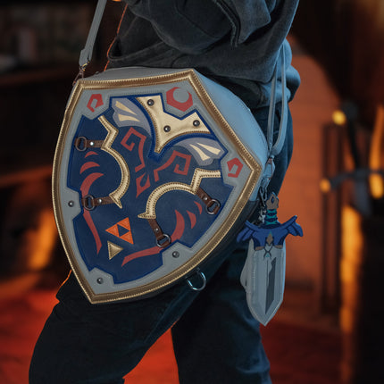 Shield-shaped bag with decorative design held by a person in a dimly lit room.