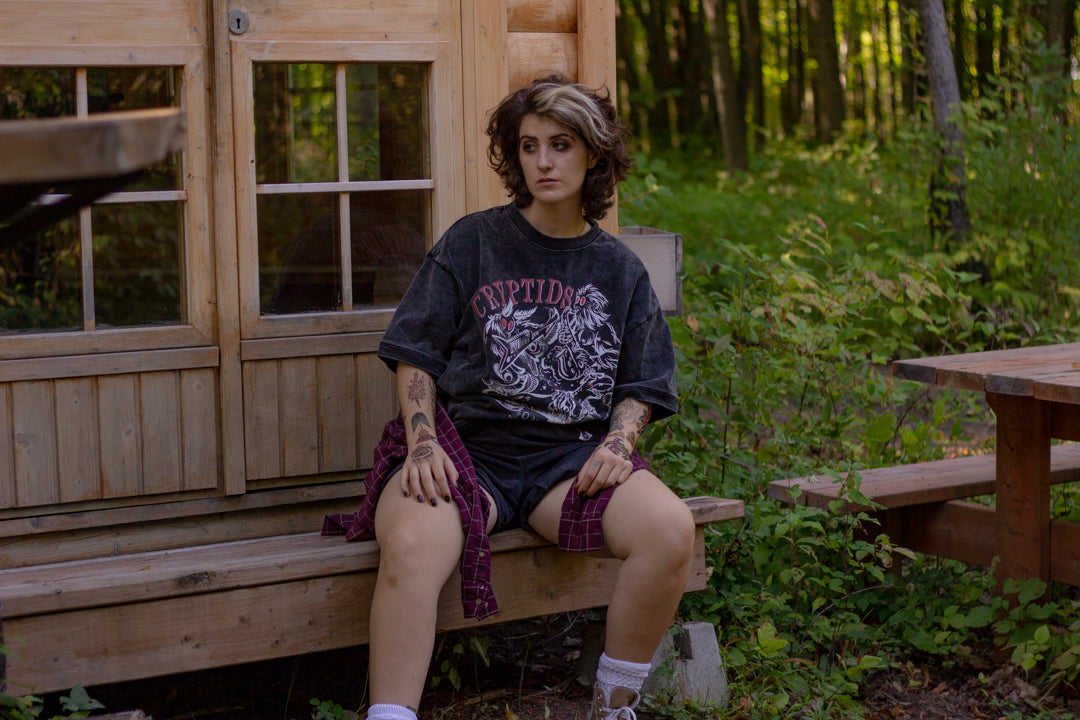 Black acid-washed oversized 80's style cotton band t-shirt with a vintage-style graphic depicting cryptids, including Bigfoot and Mothman, along with the bold text 'Cryptids On Tour' in red and white, and a list of shows across various locations and dates on the back.