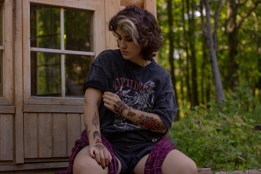 Black acid-washed oversized 80's style cotton band t-shirt with a vintage-style graphic depicting cryptids, including Bigfoot and Mothman, along with the bold text 'Cryptids On Tour' in red and white, and a list of shows across various locations and dates on the back.