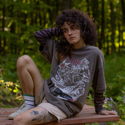 Bone-dust brown oversized cotton 80â€™s style band t-shirt with a vintage-style graphic depicting cryptids, including Bigfoot and Mothman, along with the bold text 'Cryptids On Tour' in red and white, and a list of shows across various locations and dates on the back.