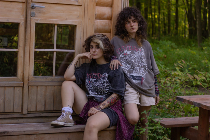 Black acid-washed oversized 80's style cotton band t-shirt with a vintage-style graphic depicting cryptids, including Bigfoot and Mothman, along with the bold text 'Cryptids On Tour' in red and white, and a list of shows across various locations and dates on the back.