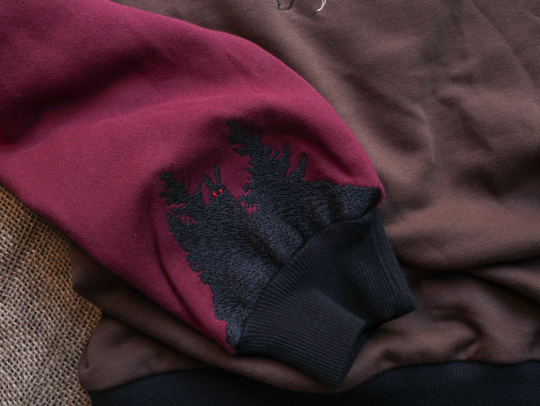 Cozy brown, green, and burgundy cotton crewneck sweatshirt, featuring a vintage, 80â€™s summer camp style embroidered design of the Mothman with cryptid-themed symbols and text.
