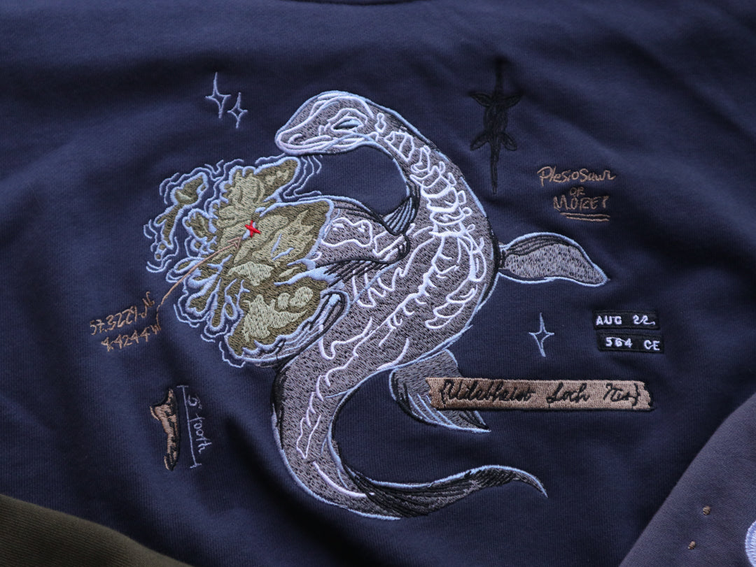 Cozy navy and fog-blue cotton crewneck sweatshirt, featuring a vintage, 80â€™s summer camp style embroidered design of the Mothman with cryptid-themed symbols and text.