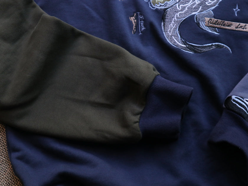 Cozy navy and fog-blue cotton crewneck sweatshirt, featuring a vintage, 80â€™s summer camp style embroidered design of the Mothman with cryptid-themed symbols and text.