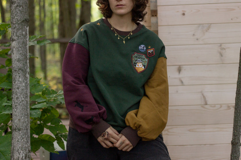 Cozy Forest green, deep yellow, and burgundy cotton crewneck sweatshirt, featuring a vintage, 80â€™s summer camp style embroidered â€œiron onâ€ patches, designed with cryptid-themed symbols and text.