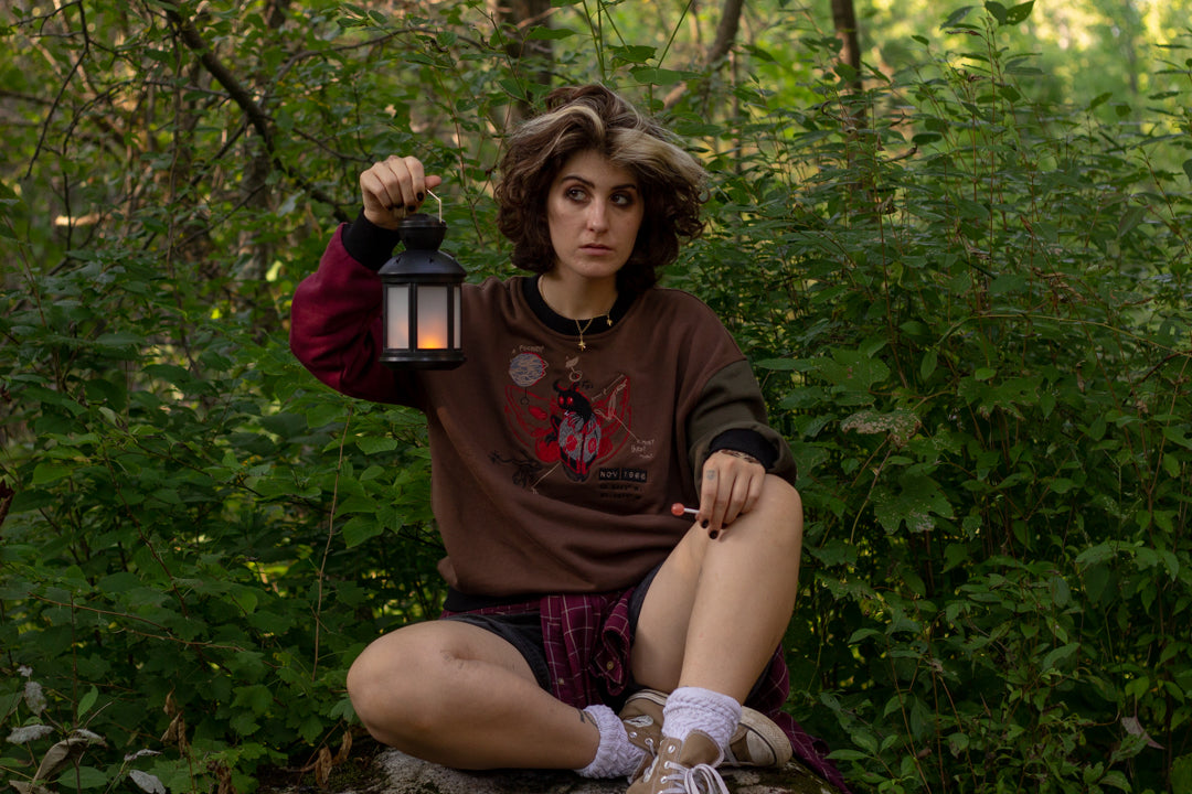 Cozy brown, green, and burgundy cotton crewneck sweatshirt, featuring a vintage, 80â€™s summer camp style embroidered design of the Mothman with cryptid-themed symbols and text.