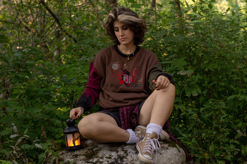 Cozy brown, green, and burgundy cotton crewneck sweatshirt, featuring a vintage, 80â€™s summer camp style embroidered design of the Mothman with cryptid-themed symbols and text.