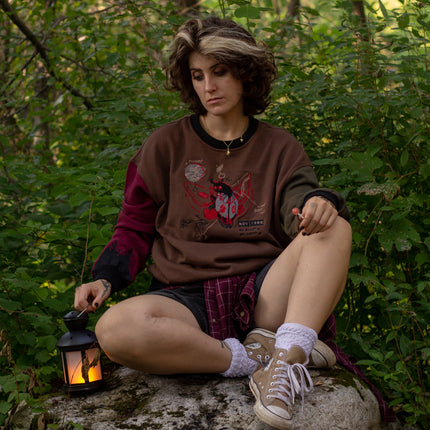 Cozy brown, green, and burgundy cotton crewneck sweatshirt, featuring a vintage, 80’s summer camp style embroidered design of the Mothman with cryptid-themed symbols and text.