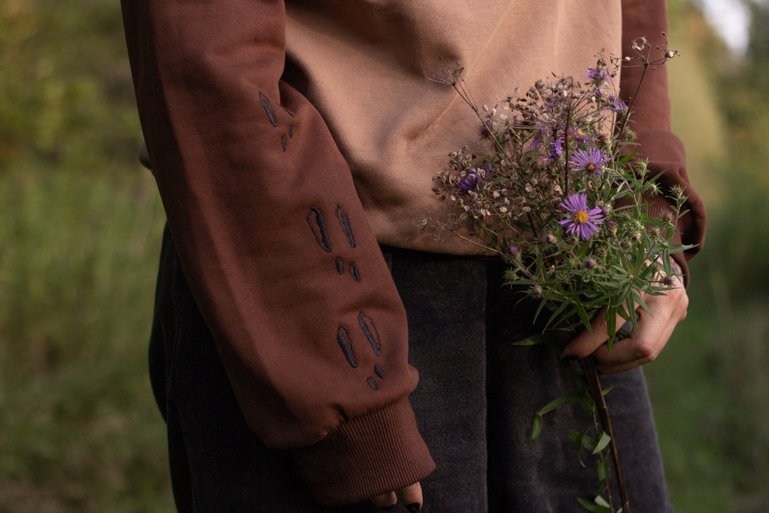 Cozy rust-orange, and peach cotton crewneck sweatshirt, featuring a vintage, embroidered design of the Jackalope with cryptid summer camp-themed symbols and text.