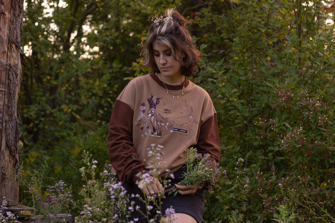 Cozy rust-orange, and peach cotton crewneck sweatshirt, featuring a vintage, embroidered design of the Jackalope with cryptid summer camp-themed symbols and text.