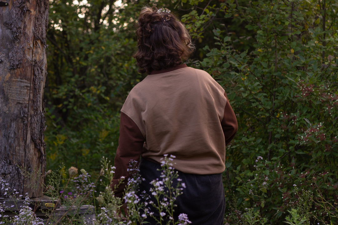 Cozy rust-orange, and peach cotton crewneck sweatshirt, featuring a vintage, embroidered design of the Jackalope with cryptid summer camp-themed symbols and text.