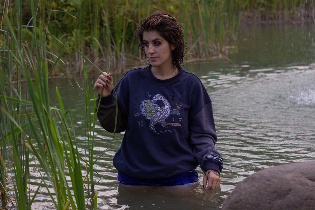 Cozy navy and fog-blue cotton crewneck sweatshirt, featuring a vintage, 80â€™s summer camp style embroidered design of the Mothman with cryptid-themed symbols and text.