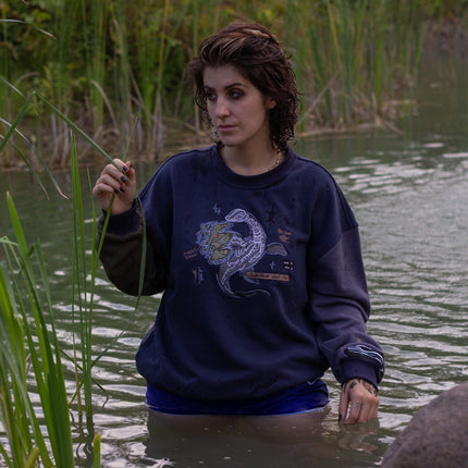 Cozy navy and fog-blue cotton crewneck sweatshirt, featuring a vintage, 80’s summer camp style embroidered design of the Mothman with cryptid-themed symbols and text.