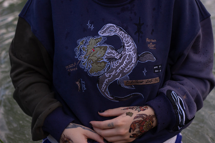 Cozy navy and fog-blue cotton crewneck sweatshirt, featuring a vintage, 80â€™s summer camp style embroidered design of the Mothman with cryptid-themed symbols and text.