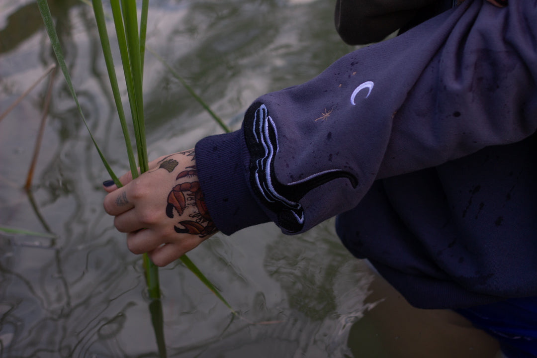 Cozy navy and fog-blue cotton crewneck sweatshirt, featuring a vintage, 80â€™s summer camp style embroidered design of the Mothman with cryptid-themed symbols and text.
