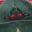 A cozy goblin-green knit wool beanie with colourful speckles, embroidered with a red-eyed, black-winged, flame-loving moth, and a glowing candle.