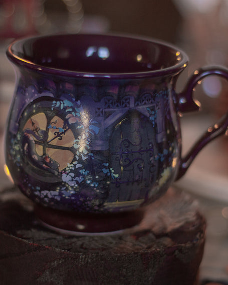 Deep plum-purple, heat-sealed 360Â° printed mug of a witchâ€™s cottage at night, featuring a mystical design with a glowing full moon, the forest glinting in the moonlight, a kitten rising for a midnight prowl, and an enchanting arched doorway. Microwave and dishwasher safe. They are a rounded shape with a wide lip, to keep your hands cozy all winter long.  